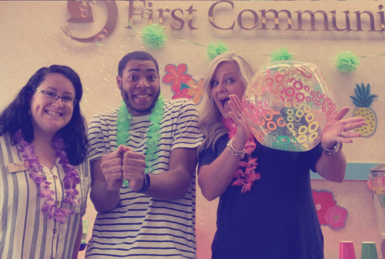 Three First Community Bank employees smiling while wearing Hawaiian leis at a party.